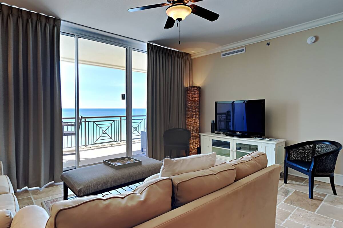 A living room with a sofa, a television, and a view of the ocean through a balcony.