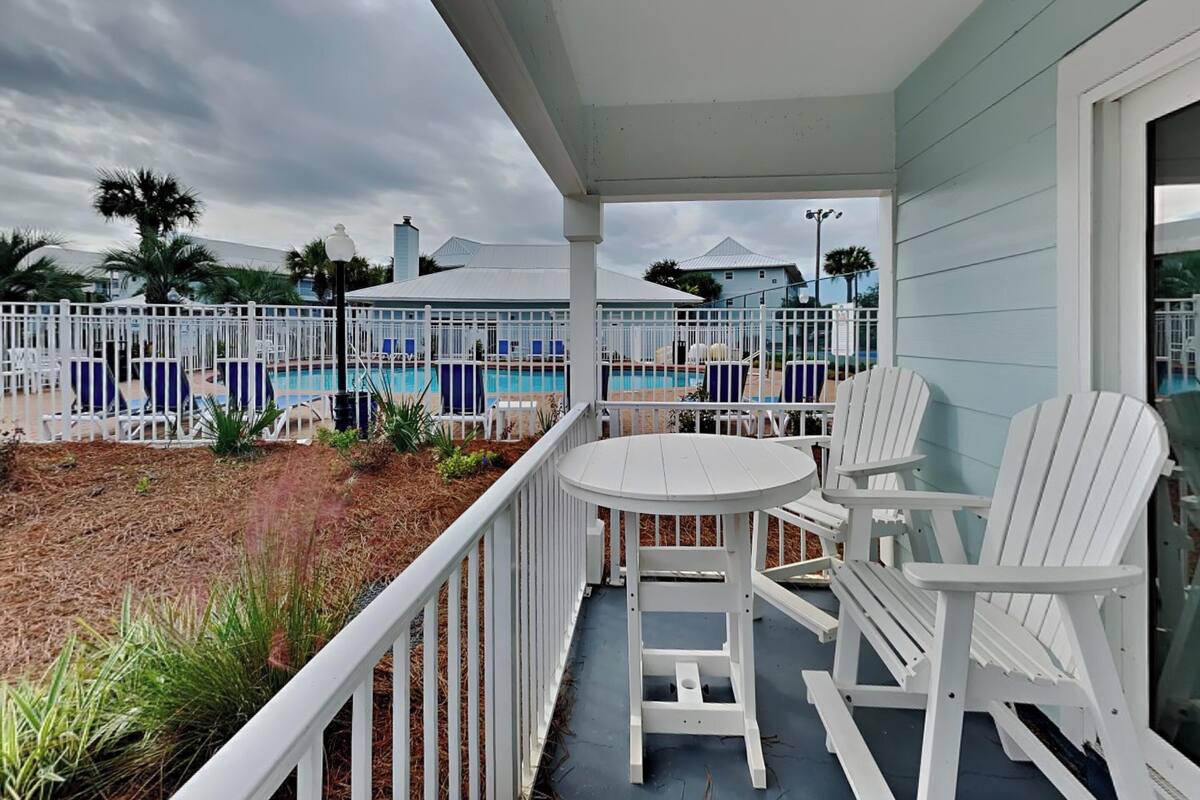 A covered outdoor area with a pool, white chairs, and a table.