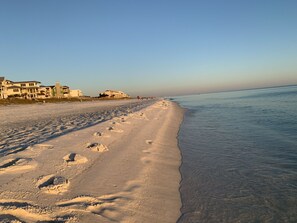 A beach with footprints leading to the water, buildings in the background, and a clear sky.