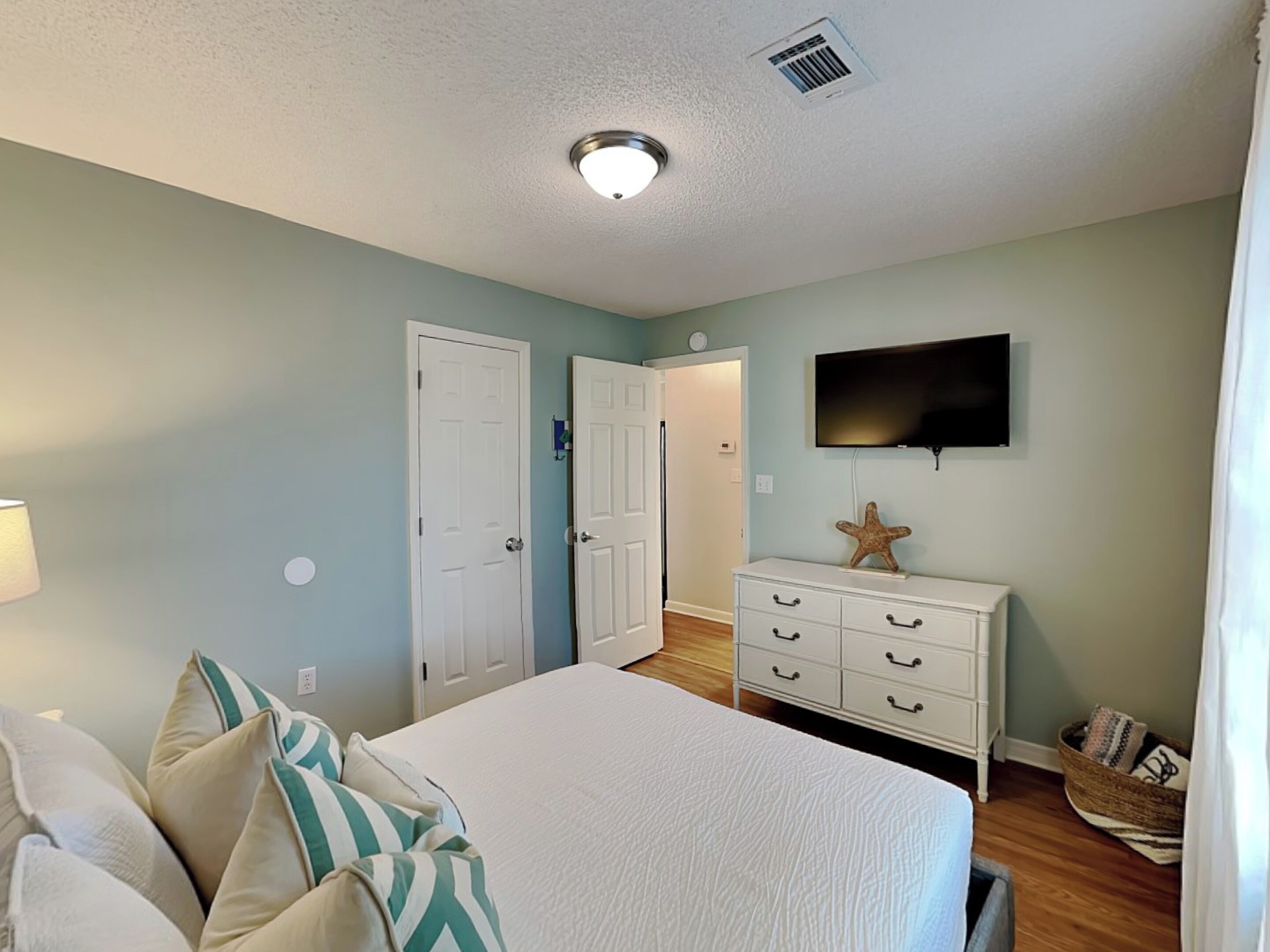 A bedroom with a bed, dresser, TV, and two doors.