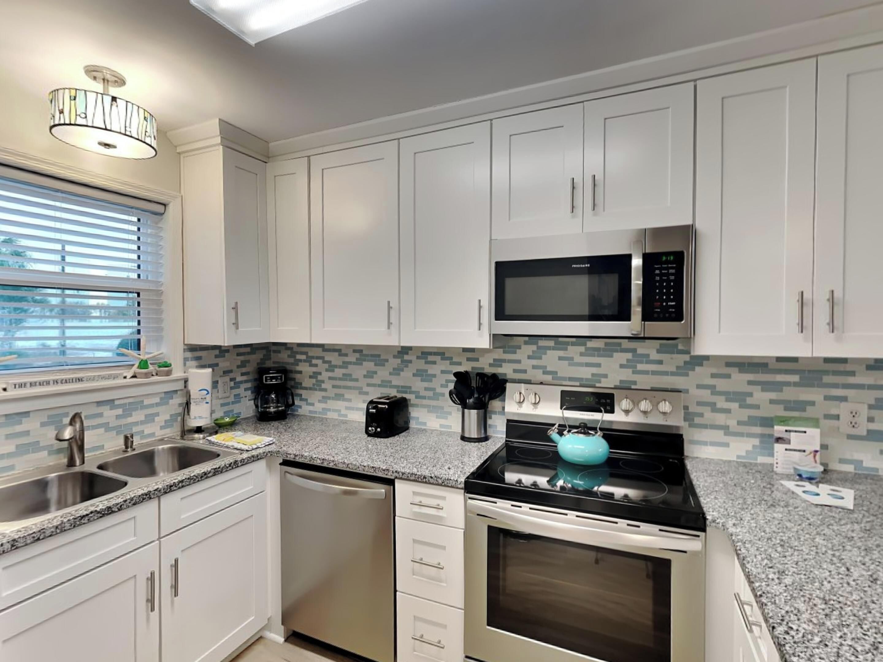 Una cocina moderna con armarios blancos, electrodomésticos de acero inoxidable, encimera de granito y ventana con persianas.