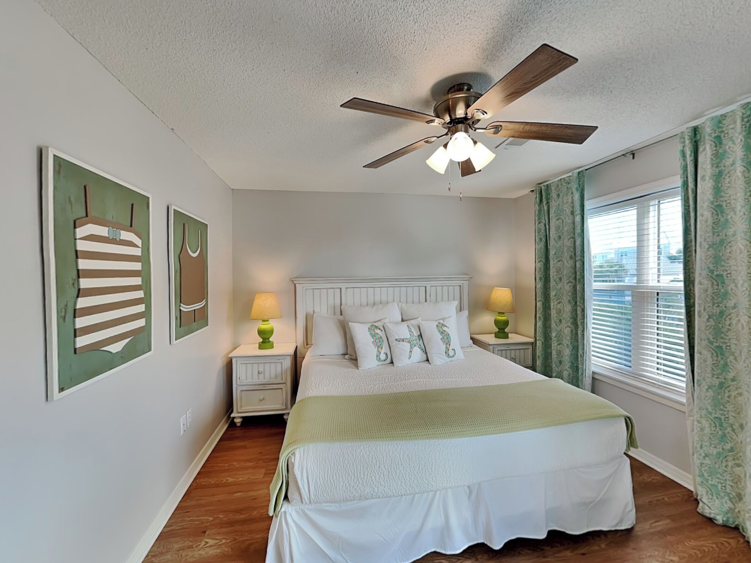 A bedroom with a bed, two bedside tables, a ceiling fan, and a window with curtains.