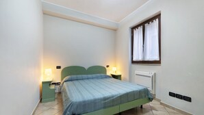 A single bed with a green headboard, two bedside lamps, a window with curtains, and a wall-mounted air conditioner.