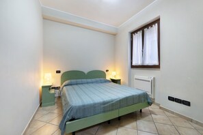 Un letto singolo con una testiera verde, due lampade sui comodini, una finestra con tende e un condizionatore d'aria fissato al muro.