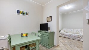 A dining area with a table, chairs, a television on a cabinet, and a sofa in the background.