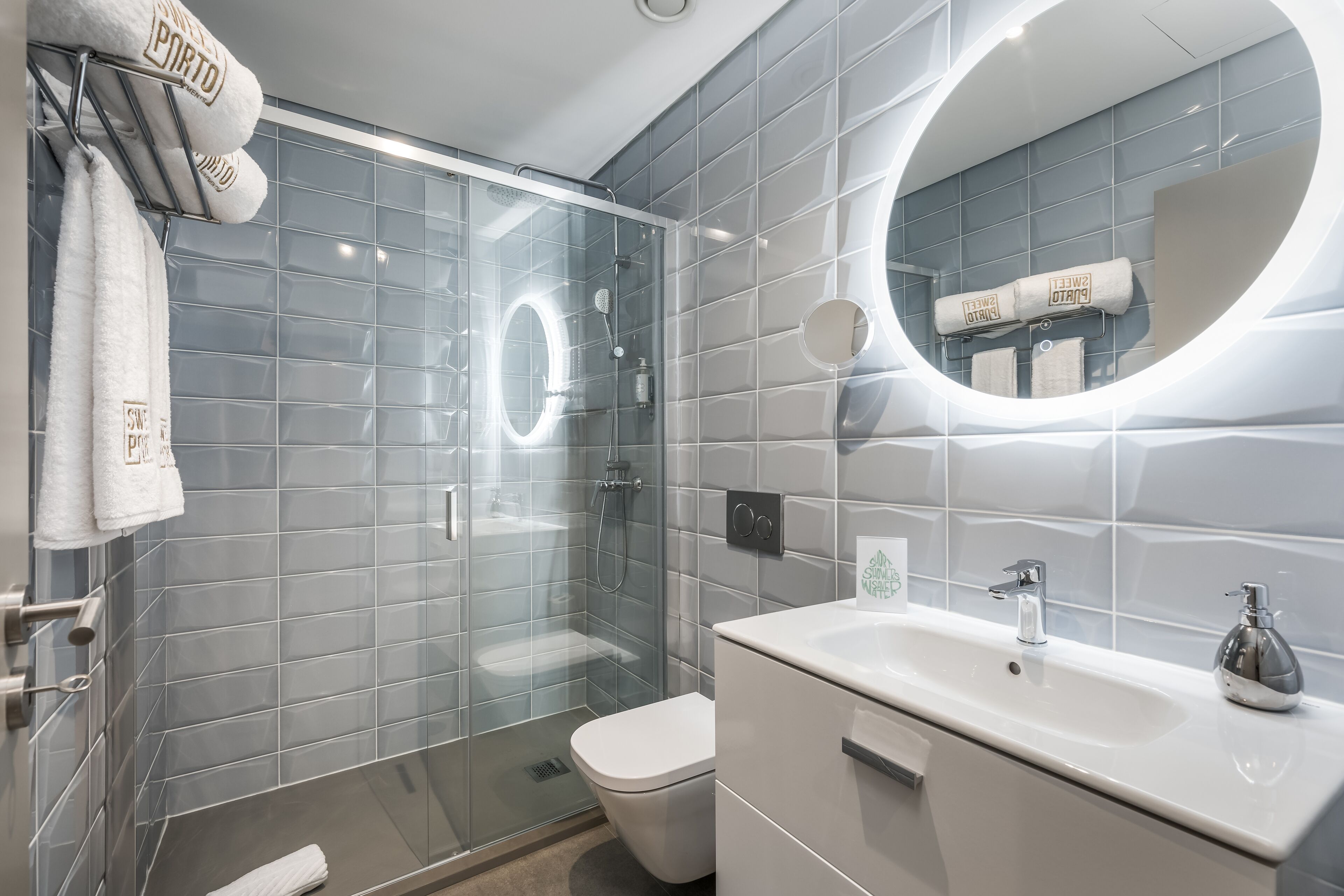 Une salle de bain moderne avec une douche à parois de verre, des toilettes blanches et un lavabo surmonté d’un miroir.