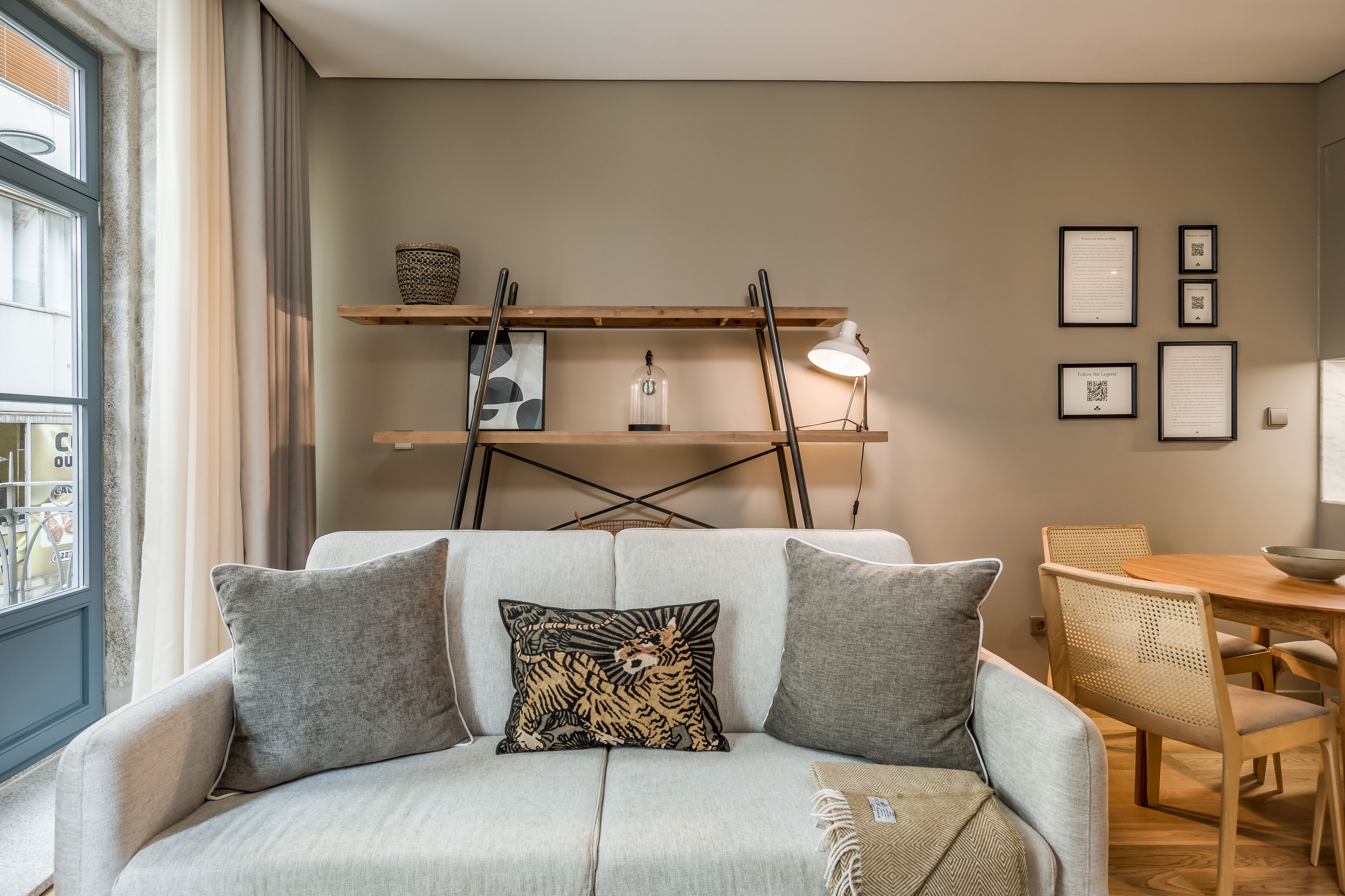A modern living room with a sofa, two pillows, a wooden dining table, and a wall-mounted shelf with decorative items.