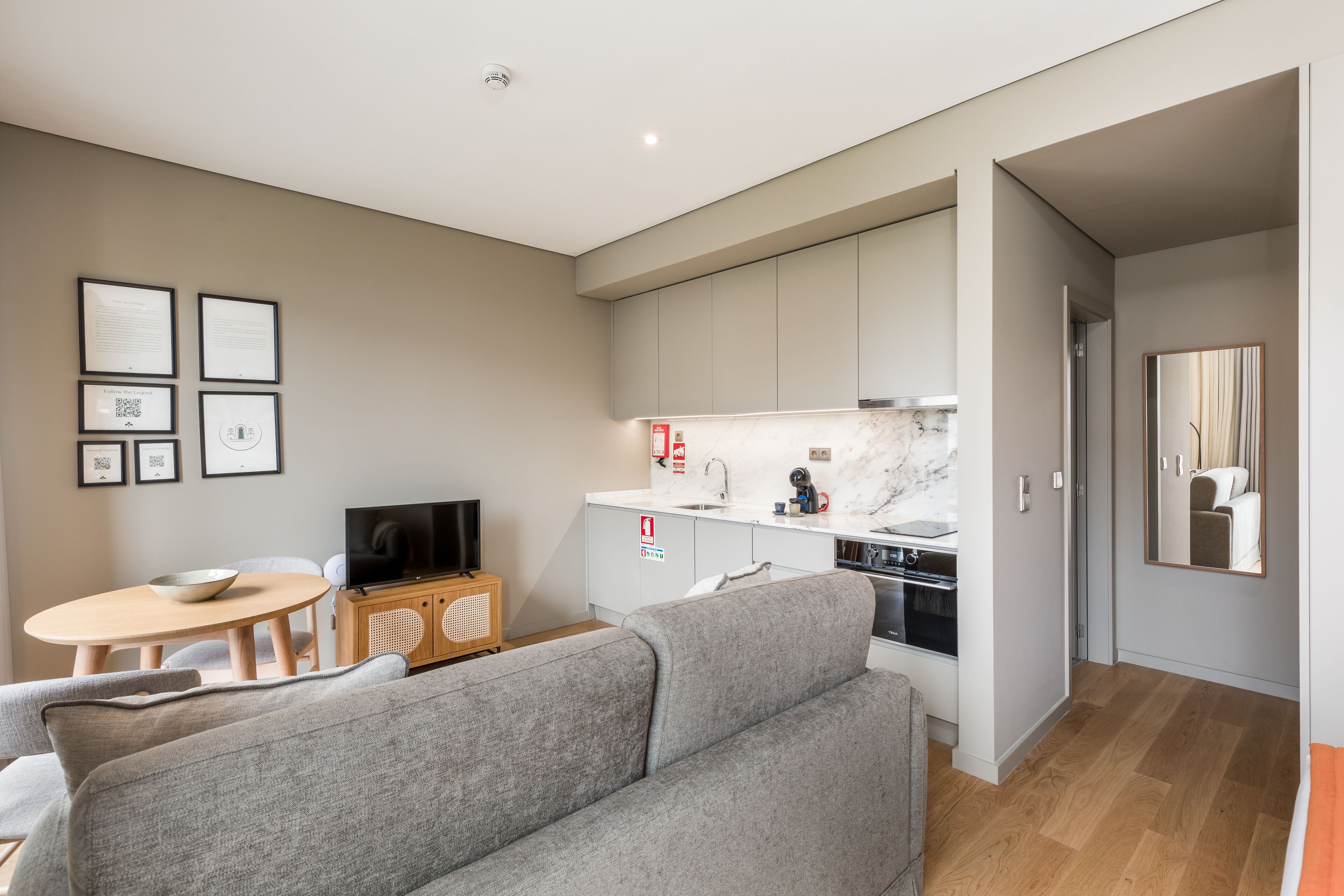 A modern apartment with a grey sofa, a dining table with chairs, a kitchen area, and a living room.