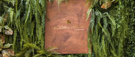 Ein Buch mit dem Titel „Legends House“ von Sweet Porto, umgeben von dichtem Grün.
