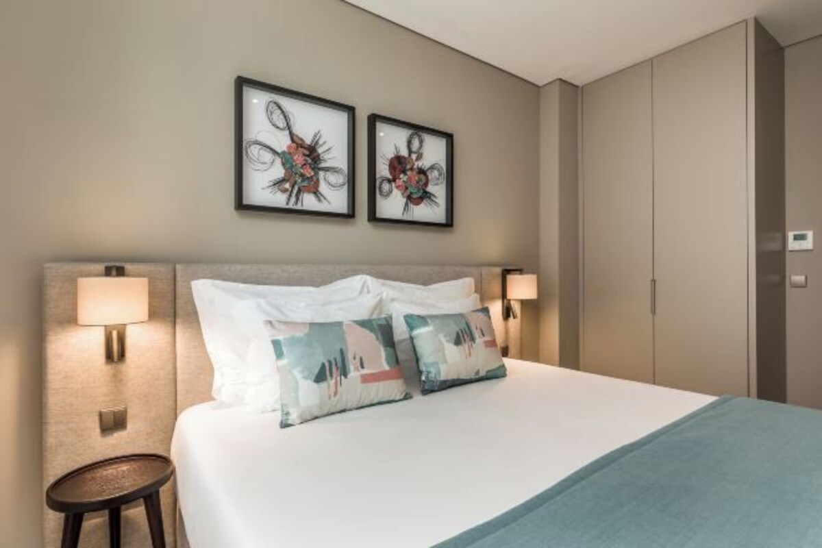 Quarto de hotel com uma cama grande, duas luminárias fixadas na parede e duas obras de arte emolduradas sobre a cama.