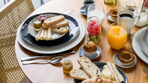 A round wooden table with breakfast items including croissants, bread, muffins, and a glass of orange juice.