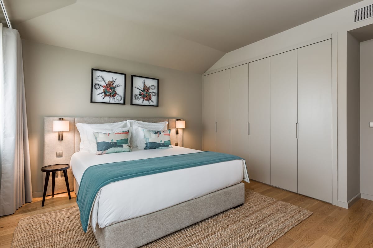 Ein modernes Schlafzimmer mit einem großen Bett, zwei Nachttischlampen, einem kleinen Beistelltisch und einem Kleiderschrank.