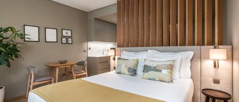 A modern hotel room with a large bed, a wooden headboard, a desk with a chair, and a small table.