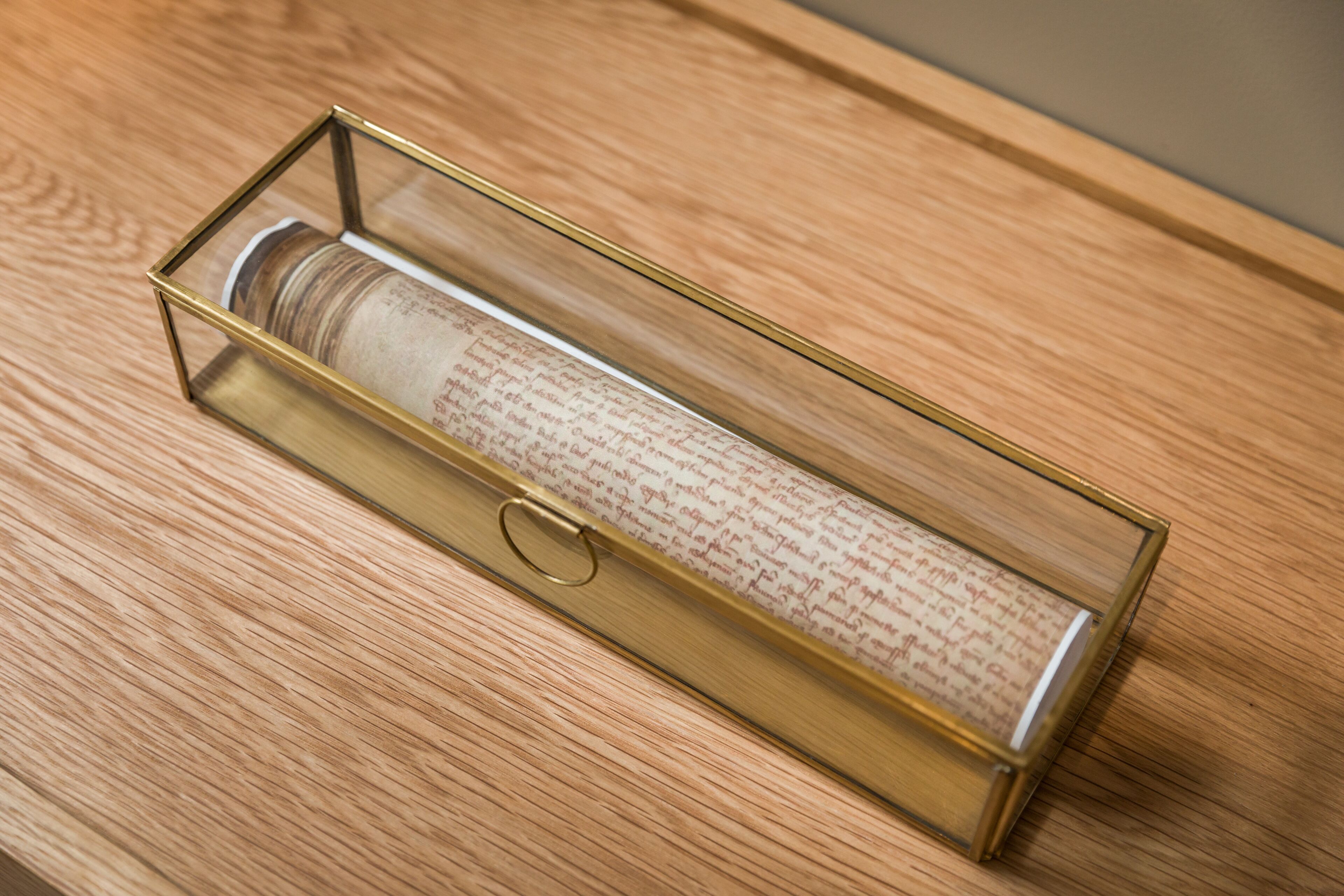 A cylindrical object in a transparent, gold-framed box on a wooden surface.