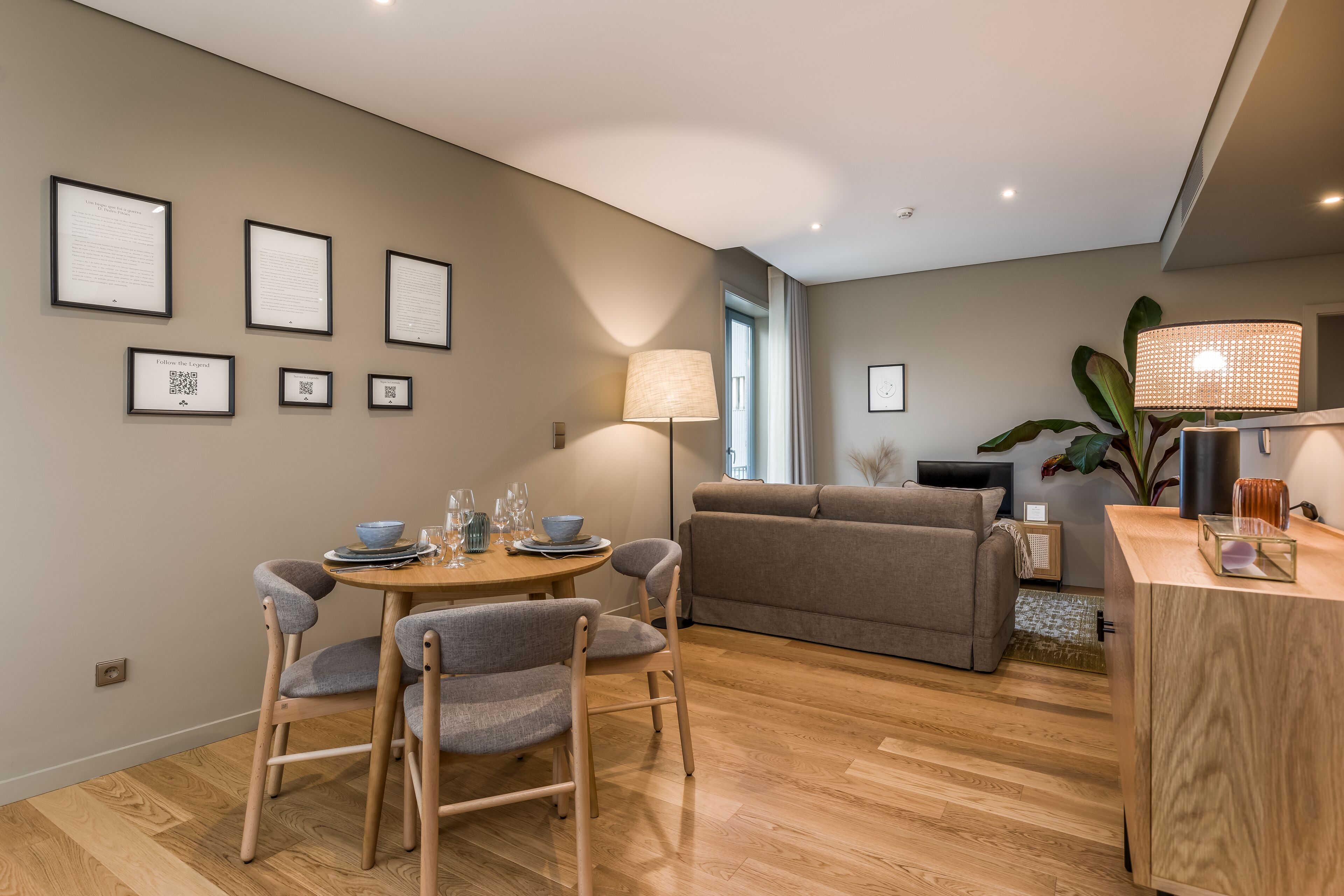 A modern living room with a dining area, featuring a sofa, chairs, a table with glasses, and framed certificates on the wall.