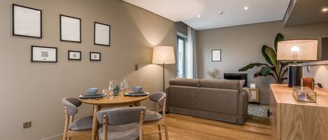 A modern living room with a dining area, featuring a sofa, chairs, a table with glasses, and framed certificates on the wall.