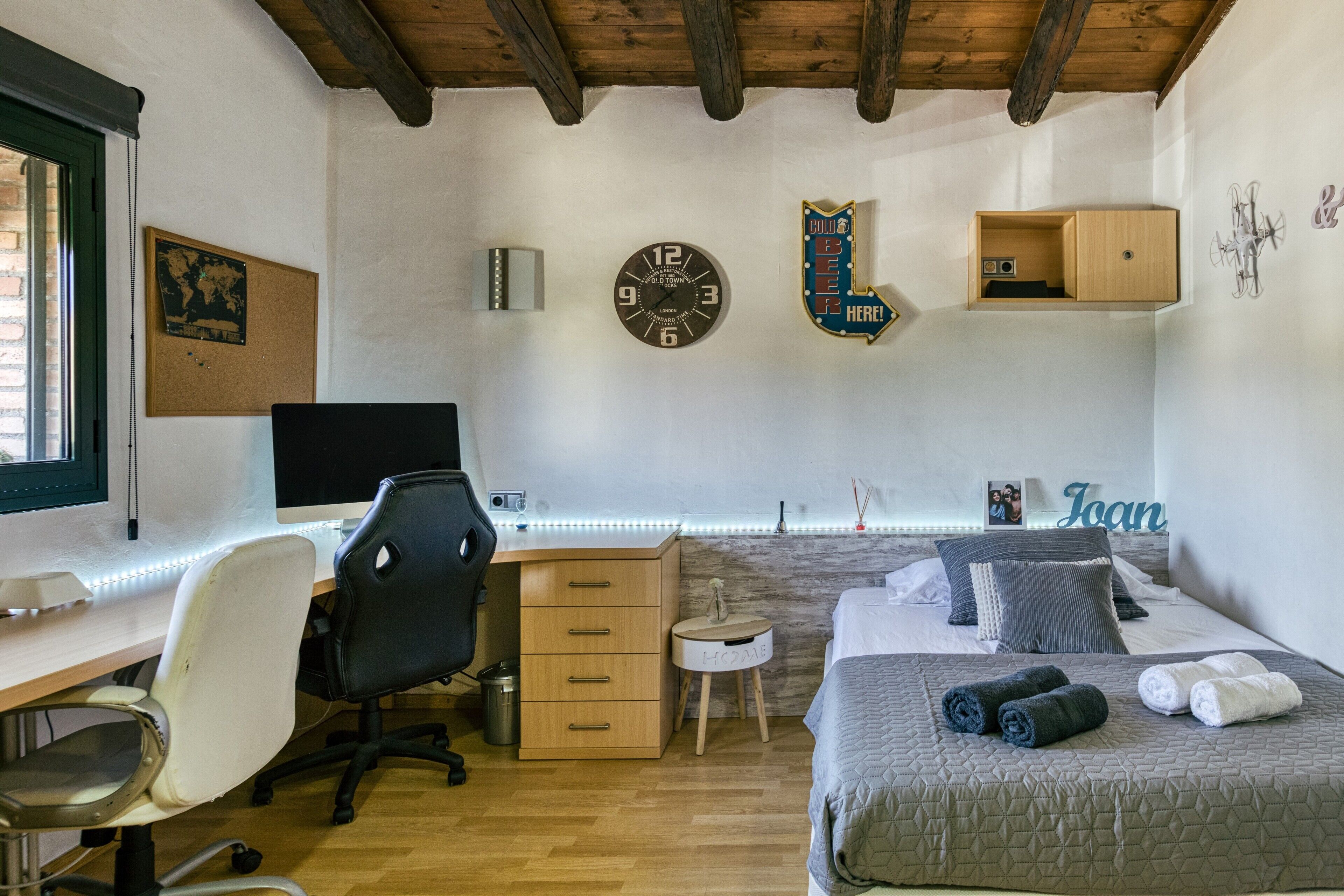 Un dormitorio con cama, escritorio, silla y un taburete pequeño.