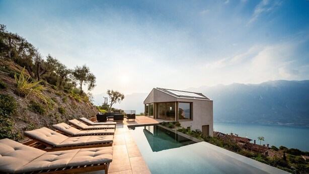 A modern house with a pool, lounge chairs, and a view of a lake and mountains. - Villa Arias with Lake View, Pool, and Wi-Fi (Tremosine sul Garda)