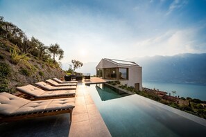 A modern house with a pool, lounge chairs, and a view of a lake and mountains. - Villa Arias with Lake View, Pool, and Wi-Fi (Tremosine sul Garda)