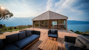A modern outdoor deck with a seating area, a glass-enclosed structure, and a scenic lake view. - Villa Arias with Lake View, Pool, and Wi-Fi (Tremosine sul Garda)