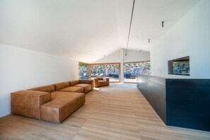 Un interior moderno con un amplio sofá seccional en forma de L, un comedor con sillas y vistas a un paisaje rocoso a través de grandes ventanales.