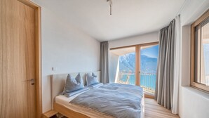 A bedroom with a bed, a wooden door, a window with curtains, and a view of mountains. - Villa Arias with Lake View, Pool, and Wi-Fi (Tremosine sul Garda)