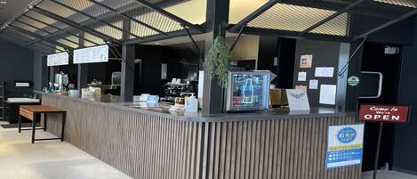 Una recepción con diseño moderno, un cartel que indica que el lugar está abierto y una pizarra de menú visible detrás del mostrador.