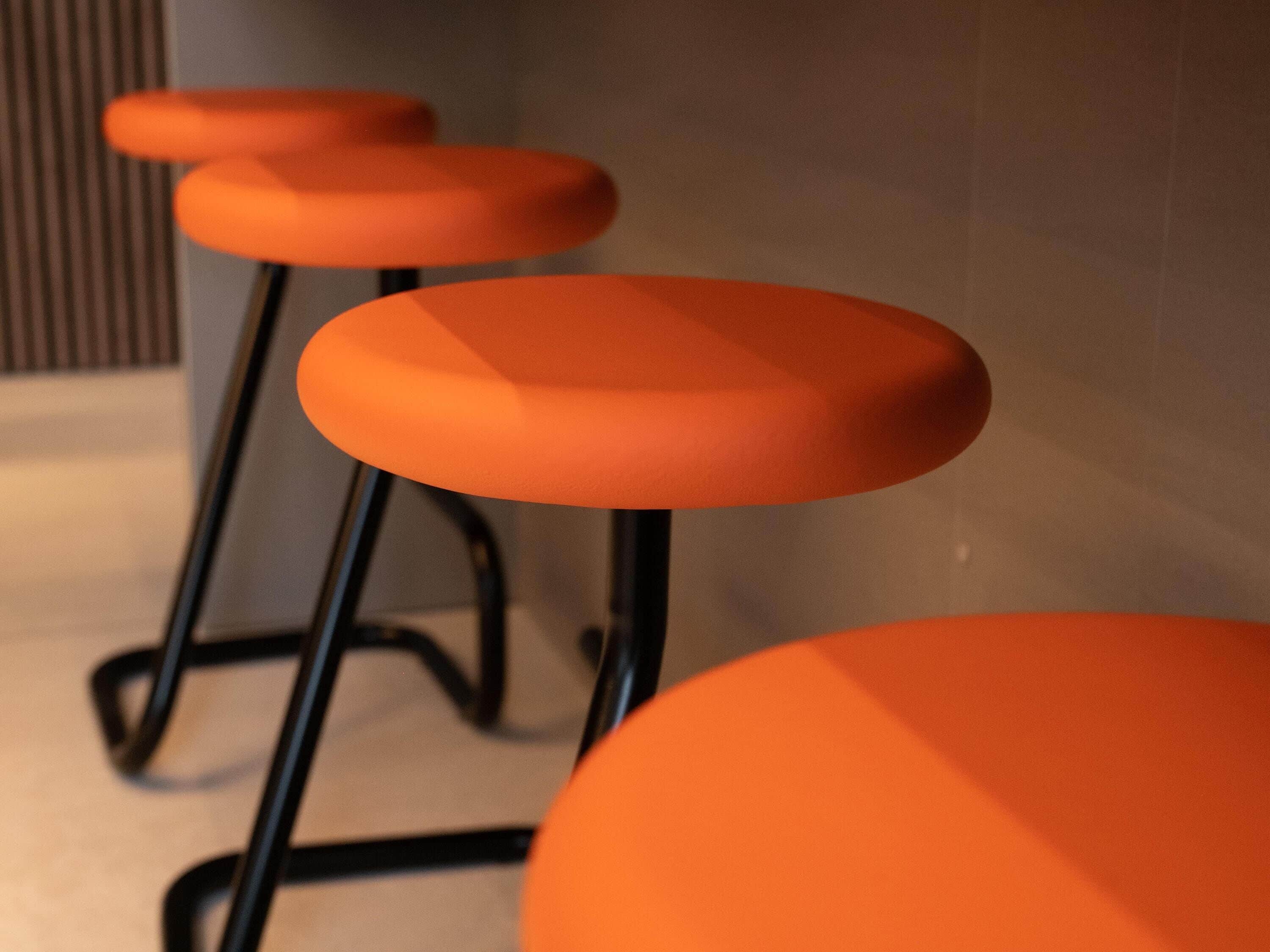 Tres taburetes naranja con patas de metal negro.