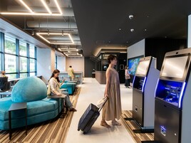 Um hall de hotel moderno com áreas de estar, balcão de recepção e totens de autoatendimento.