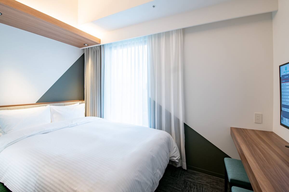 A hotel room with a large bed, a desk, and a window with curtains.