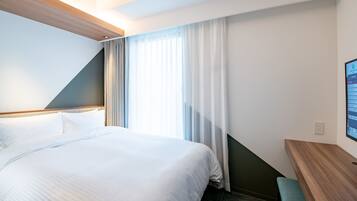 A hotel room with a large bed, a desk, and a window with curtains.