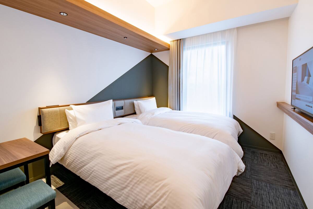 A hotel room with two beds, a desk, and a TV.