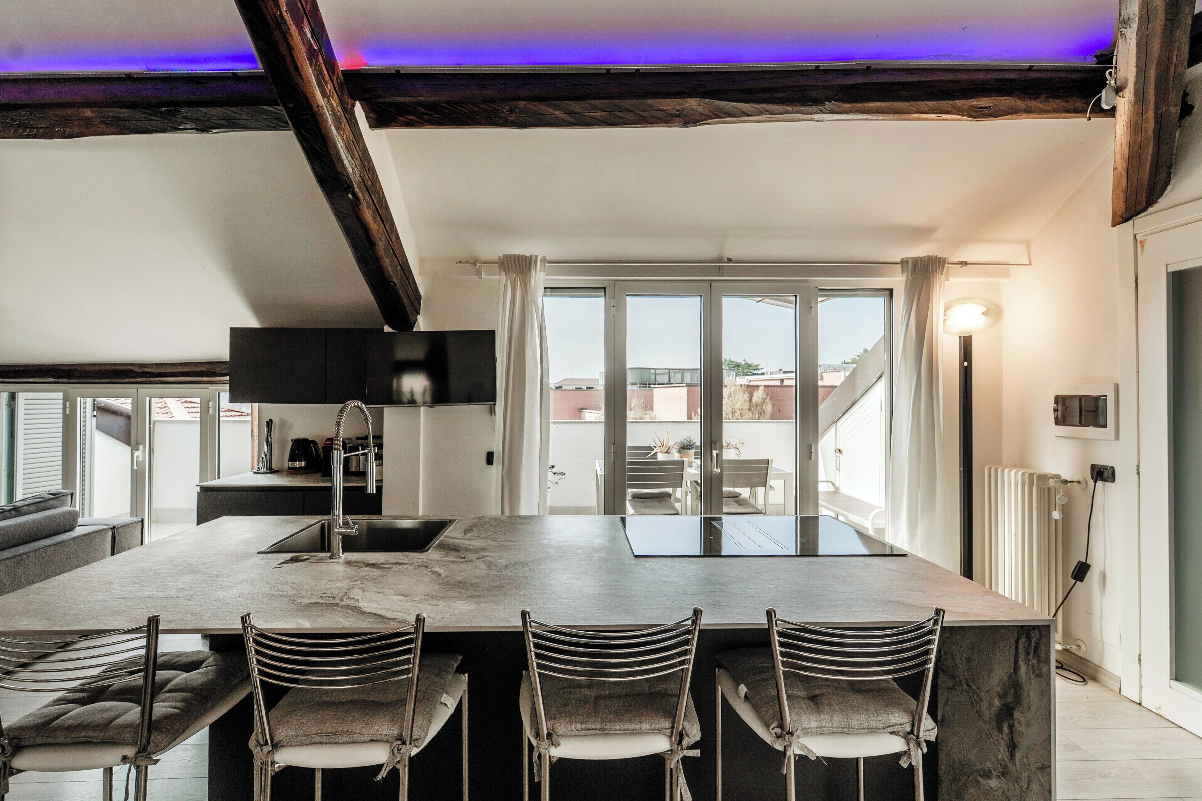 A modern kitchen with a marble countertop, bar stools, and a large window.