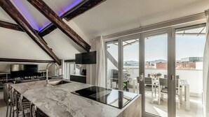 Une cuisine moderne dotée d’un plan de travail en marbre, de tabourets de bar, d’un four encastré et d’une grande fenêtre donnant sur la ville.