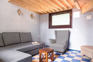 Une pièce avec un canapé gris, un fauteuil à carreaux, une petite table en bois et une fenêtre avec des stores.