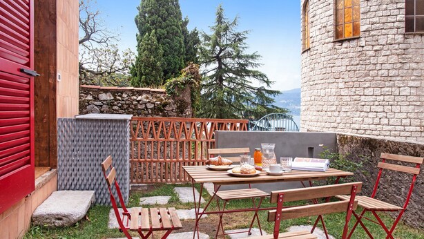 Un espace extérieur aménagé pour les repas, avec un mur en pierre, du mobilier en bois et une vue sur le paysage.