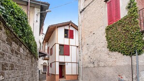 Une rue étroite, bordée de bâtiments des deux côtés, dont les façades présentent un mélange de murs en briques et en crépi, certains agrémentés de volets rouges.