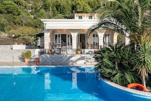 A poolside area with a clear blue pool, a building with a stone facade, and a palm tree.