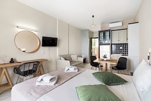 A hotel room with a bed, a desk, a chair, a TV, and a kitchenette.