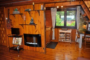 Un interior de cabaña acogedor con detalles de madera, una chimenea, un comedor y una ventana con vistas a zonas verdes.