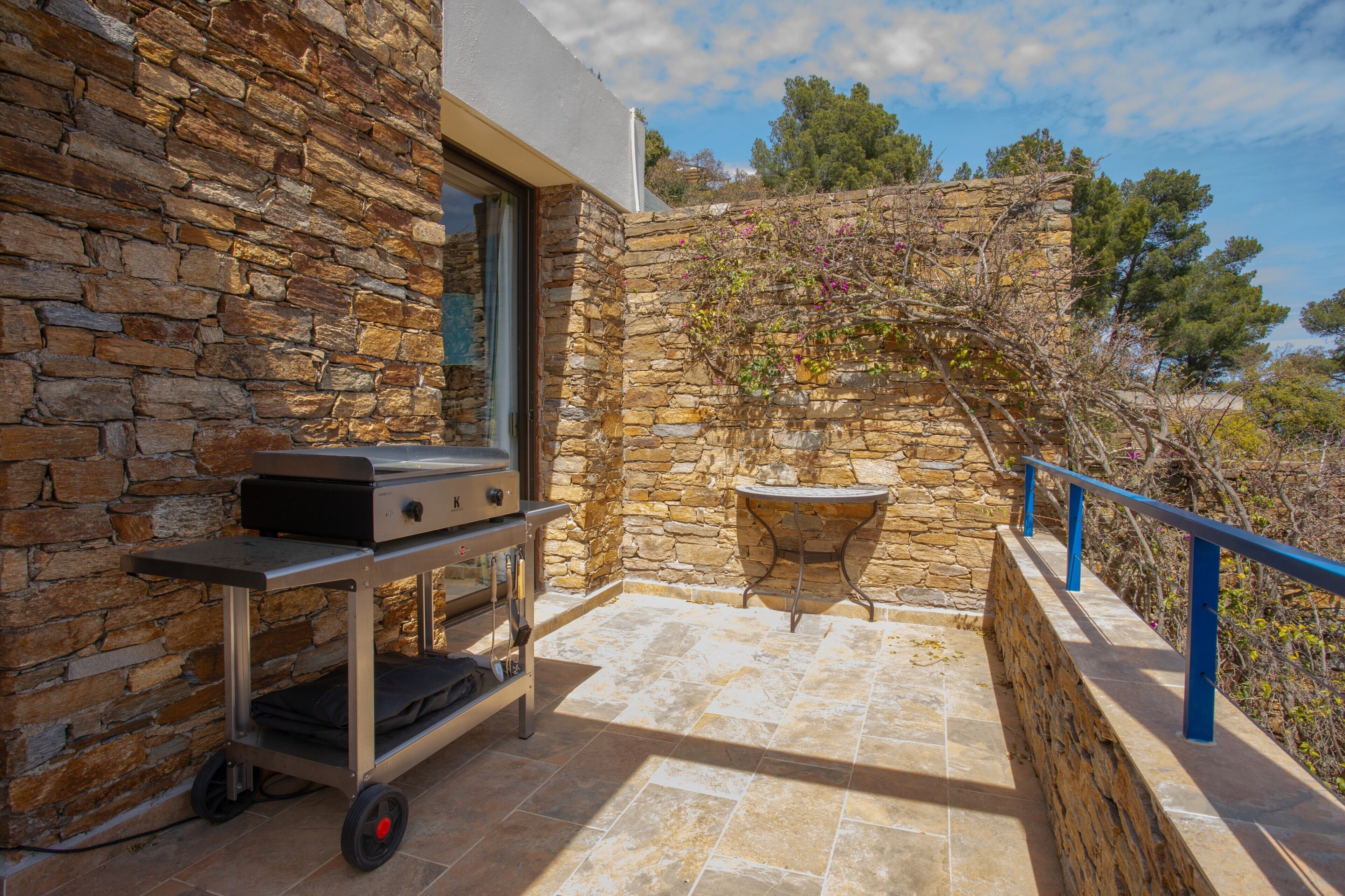Un bâtiment en pierre avec un chariot-grill, une petite table et une rambarde.