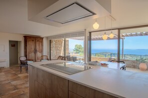 Een moderne keuken met een groot eiland, stenen muren en uitzicht op zee.
