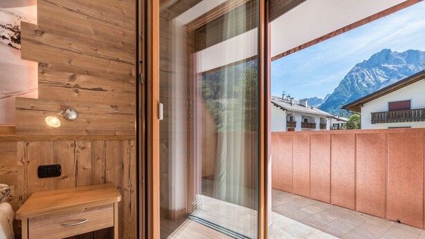 A wooden interior with a sliding glass door leading to a balcony with a mountain view. - Apartment Ciasa Rosa with Mountain View, Balconies & Shared Garden (Canazei)