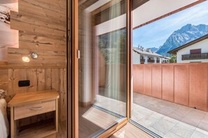 A wooden interior with a sliding glass door leading to a balcony with a mountain view.