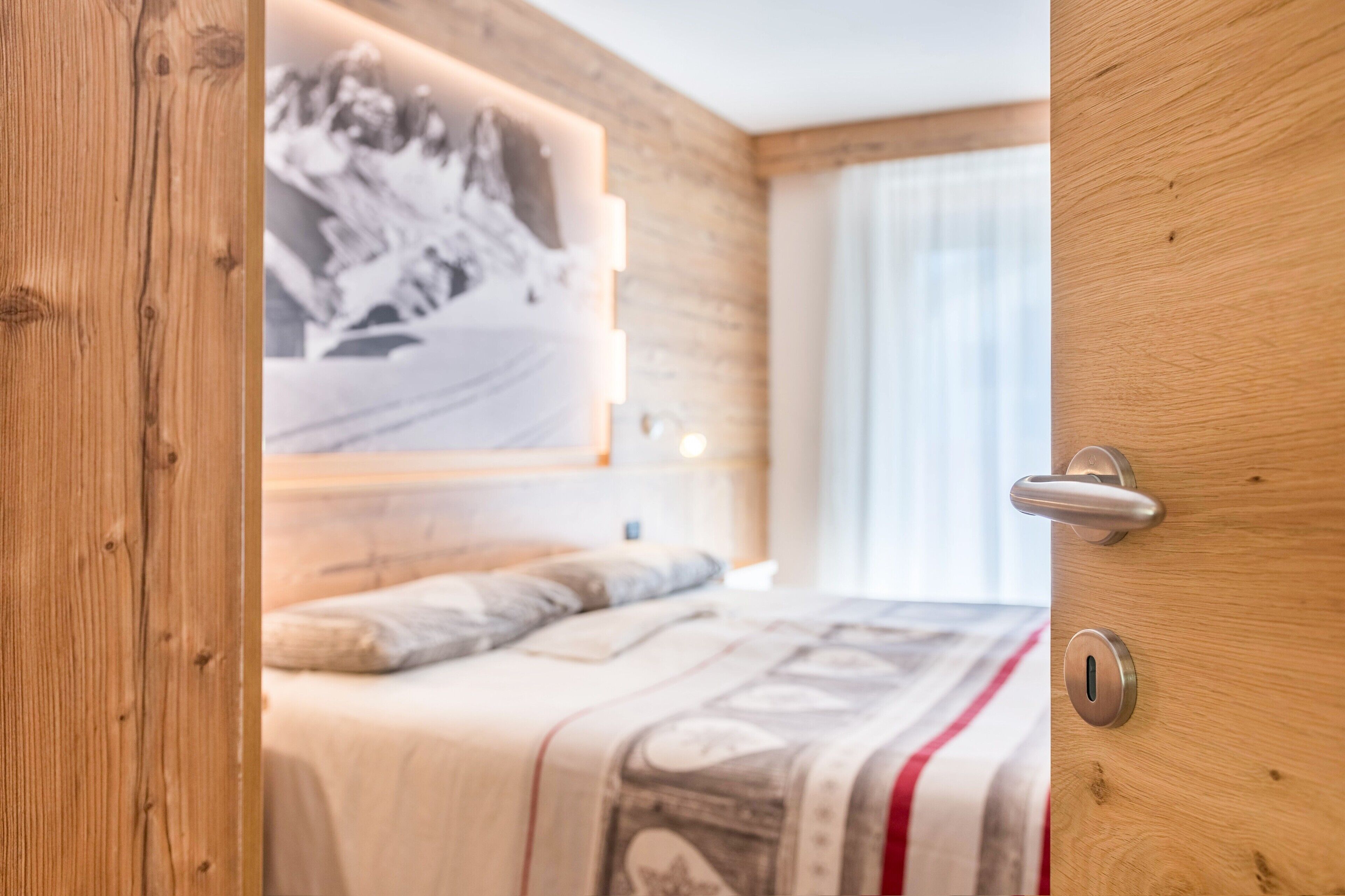 A bedroom with a bed, a wall-mounted light, a door with a handle, and a window with curtains.