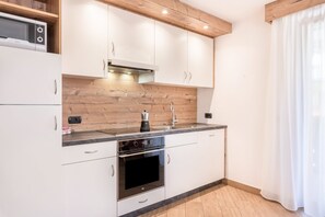 A modern kitchen with white cabinets, a wooden countertop, a built-in microwave, and a coffee maker. - Apartment Ciasa Rosa with Mountain View, Balconies & Shared Garden (Canazei)
