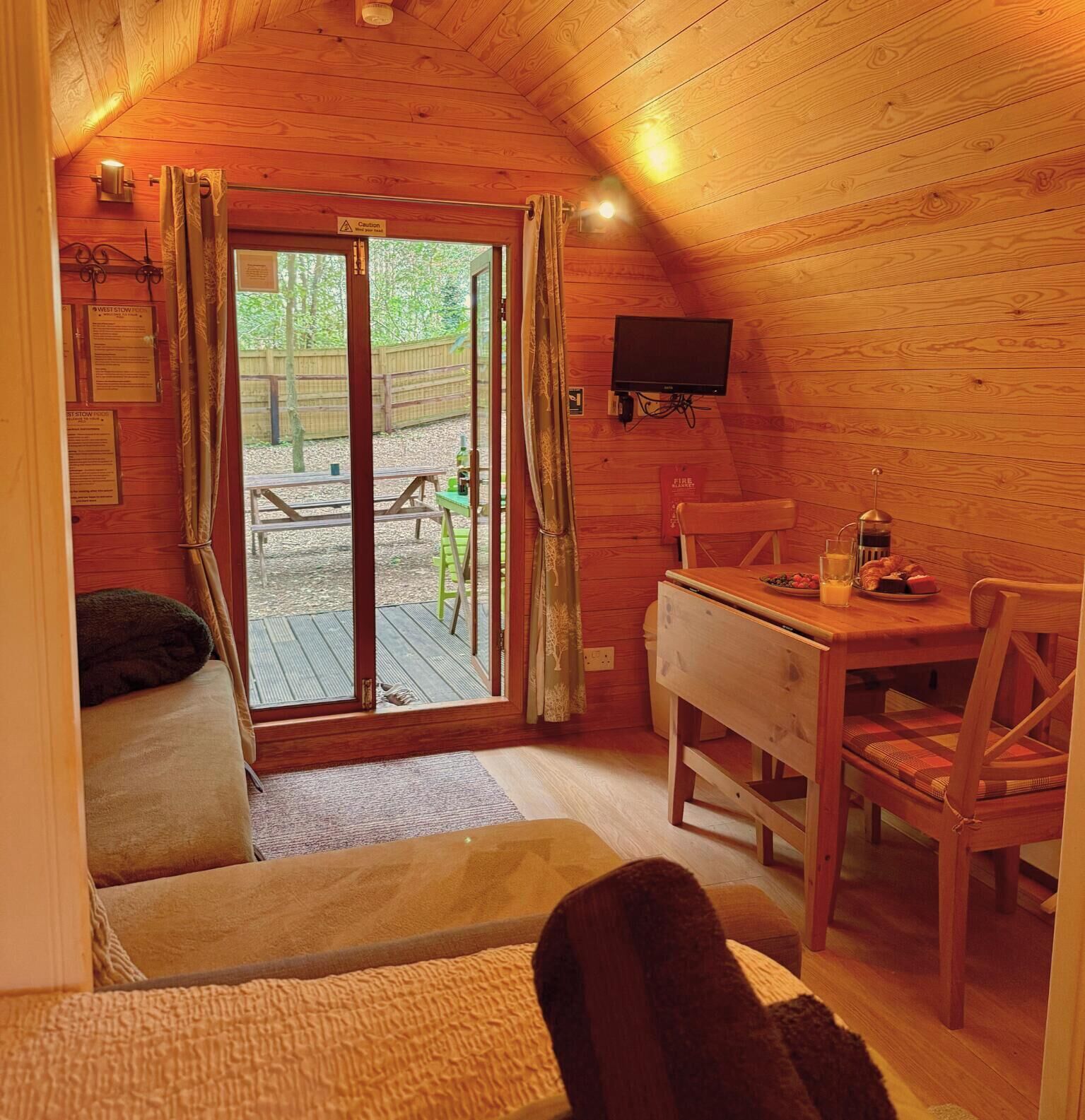 Een gezellig houten interieur met een houten plafond, een eettafel met stoelen, een bank en een aan de muur bevestigde televisie.