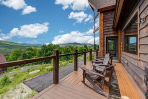 Una terraza de madera con asientos al aire libre, con vistas a un paisaje pintoresco de colinas y cielo despejado.