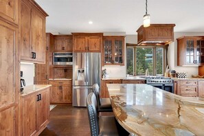 Una cocina con armarios de madera, electrodomésticos de acero inoxidable, una isla de mármol y un amplio ventanal.