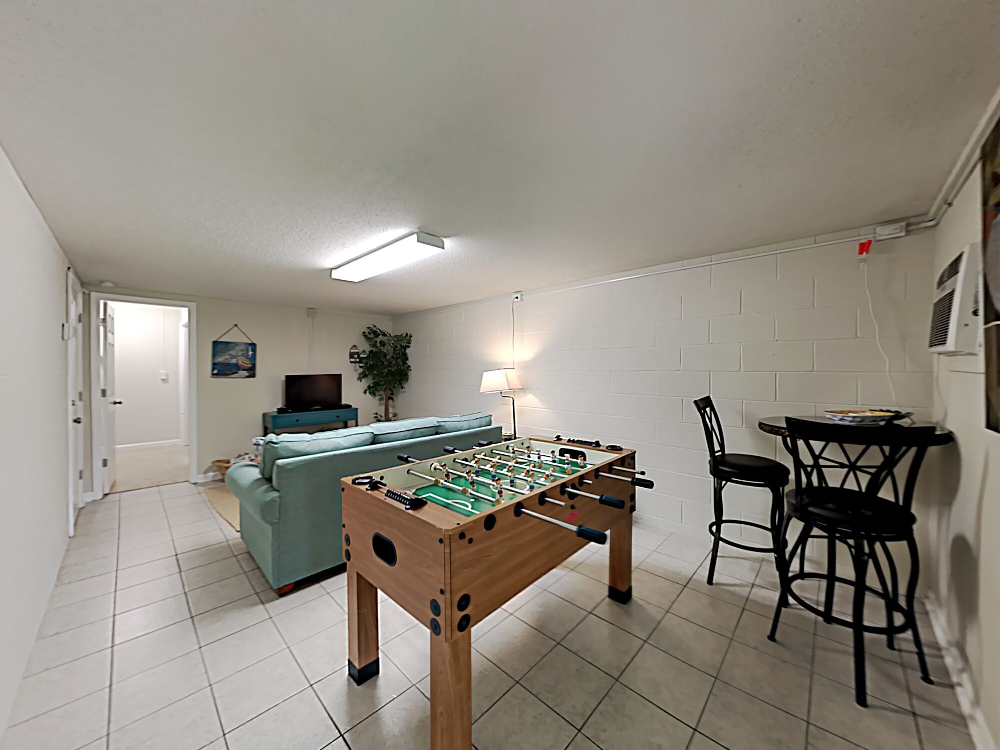 Une pièce comprenant une table de baby-foot, un canapé, un téléviseur et un coin repas avec des chaises et une table.